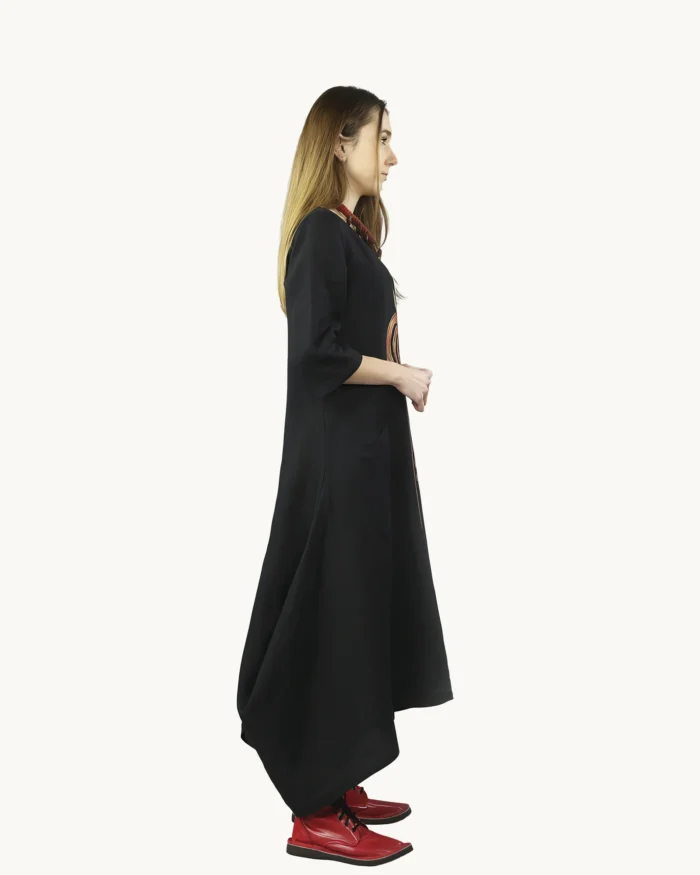 Czarna lniana sukienka oversize o luźnej, swobodnej formie z wyraźnie zaznaczoną asymetrią dołu, ozdobiona ręcznie malowanymi wzorami, widok z boku