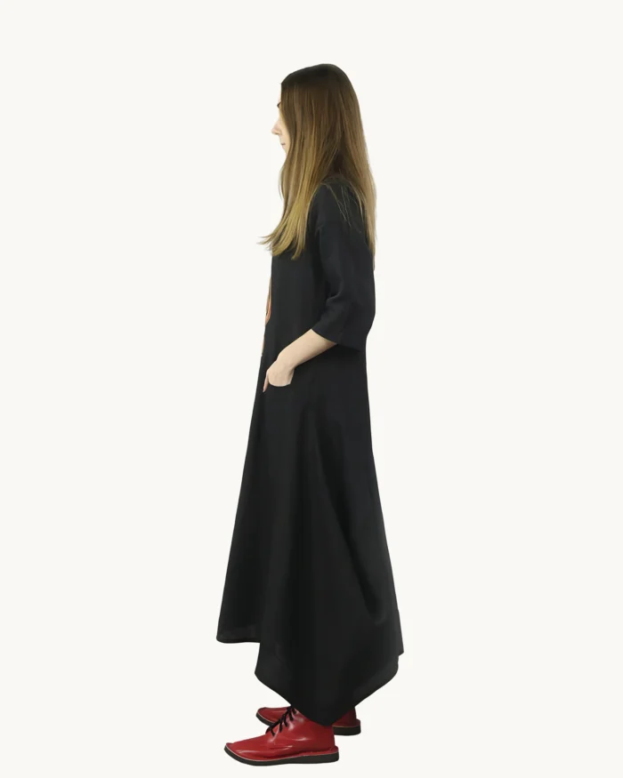 Czarna lniana sukienka oversize o luźnej, swobodnej formie z wyraźnie zaznaczoną asymetrią dołu, ozdobiona ręcznie malowanymi wzorami, widok z boku