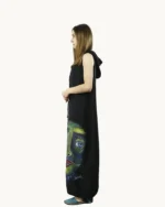 Czarna długa lniana sukienka oversize z kapturem z kieszeniami, bez rękawów, ozdobiona ręcznie malowaną abstrakcyjną twarzą, widok z boku