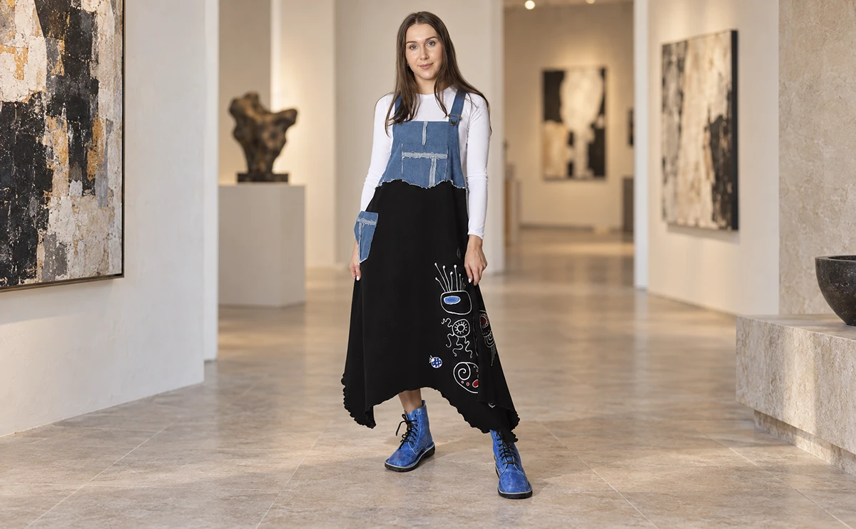 Modelka w ręcznie malowanej sukience ogrodniczce z jeansu i czarnej dzianiny we wnętrzu galerii