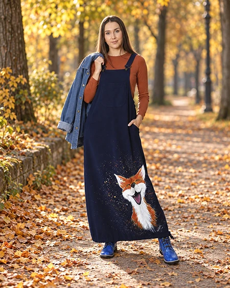 Modelka w granatowej sukience ogrodniczce z malowanym lisem, rudej bluzce i jeansowej kurtce na ramieniu w jesiennym parku